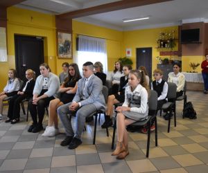 Zdjęcie przedstawia młodzież i dorosłych słuchających recytacji.