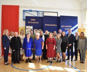 Nauczyciele szkoły i zaproszeni goście na tle tablicy dekoracyjnej