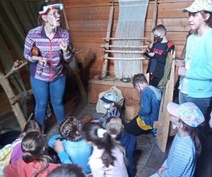 Dzieci w chacie gockiej słuchają pracowniczki muzeum. Oglądają warsztat tkacki