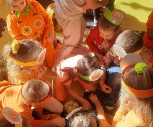 Dzieci siedzą w kole na macie i próbują pestek dyni.