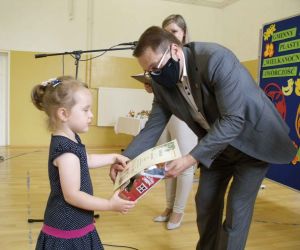 Mężczyzna wręcza dziewczynce w granatowej sukience dyplom i nagrodę