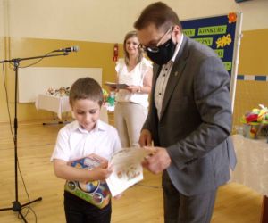 Mężczyzna wręcza dyplom i nagrodę chłopcu w białej koszuli