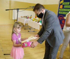 Mężczyzna wręcza dyplom i nagrodę dziewczynce w różowej sukience