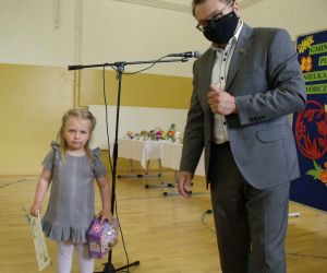 Mężczyzna i dziewczynka w szarej sukience. Dziewczynka trzyma w rękach dyplom i nagrodę