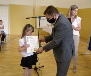 Mężczyzna wręcza dyplom i nagrodę dziewczynce w białej bluzce i czarnej spódniczce