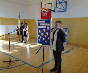 Uczeń w stroju galowym recytuje przy mikrofonie