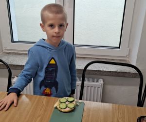 Chłopiec stoi przy stoliku, a na nim leży kanapka.