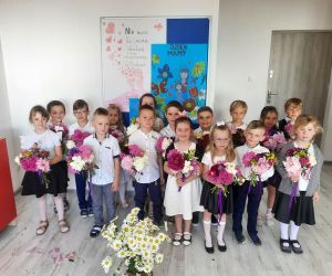 Przedszkolaki w eleganckich ubraniach trzymają w rękach bukiety kwiatów