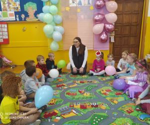 Dzieci siedzą w kole wraz z nauczycielką. Poznają andrzejkowe wróżby.