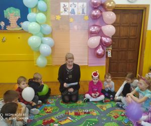 Dzieci siedzą w kole wraz z nauczycielką. Poznają andrzejkowe wróżby.