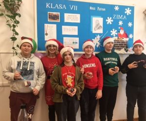 Uczniowie klasy VII z wychowawczynią, w czapkach mikołajkowych stoją przed ścianą