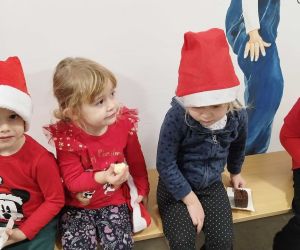 Przedszkolaki siedzące na ławeczce degustują ciasteczka