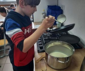 Chłopiec w czerwonej bluzie wlewa ciasto naleśnikowe na patelnię