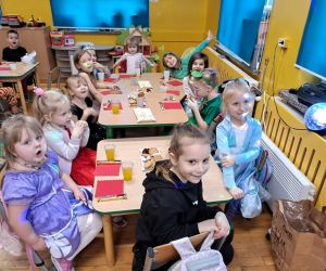 Dzieci siedzą przy stolikach i delektują się słodkimi przystawkami.