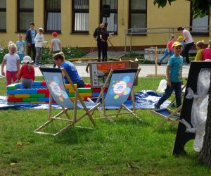 Rozstawione leżaki na na trawie, obok bawią się dzieci