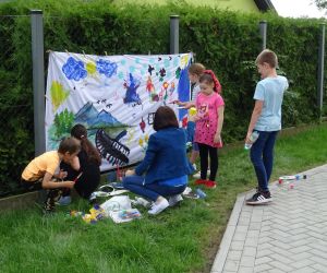 Dzieci malują na białym materiale rozwieszonym na płocie