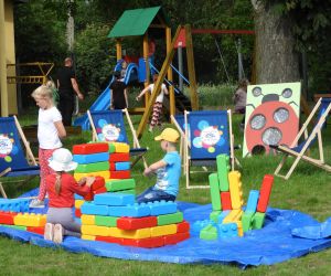 Na niebieskiej plandece dzieci bawią się ogromnymi klockami