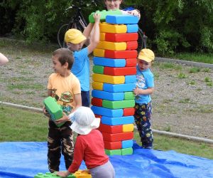 Na niebieskiej plandece dzieci bawią się ogromnymi klockami
