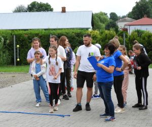 Grupa ludzi stoi obok siebie, dzieci czekają na swoją kolej w grze, dorośli pilnują zasad