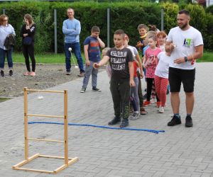 Grupa ludzi stoi obok siebie, dzieci czekają na swoją kolej w grze, dorośli pilnują zasad
