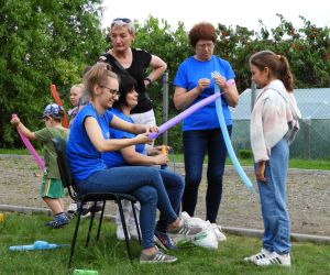Kobiety mają w rękach długie balony, dziecko stoi  i czeka