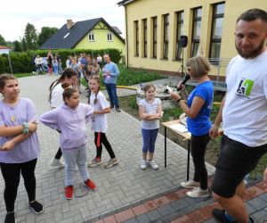 Grupa dzieci stoi przed panią, słuchają co do nich mówi