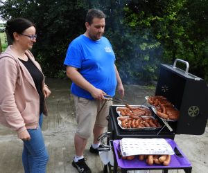 Kobieta i mężczyzna stoją przy grillu, pieką kiełbaski