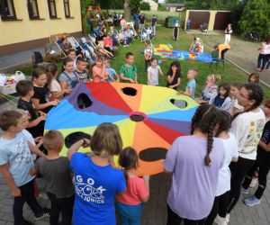 Dzieci stoją dookoła kolorowej, wielkiej chusty, bawią się