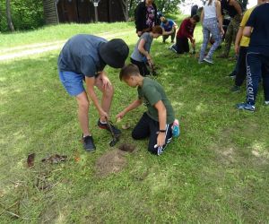 Dzieci znajdują się na świeżym powietrzu, kopią w parach dołki, w których będą rozpalały ogień.