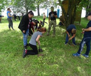 Dzieci znajdują się na świeżym powietrzu, kopią w parach dołki, w których będą rozpalały ogień.