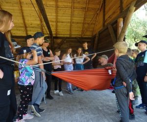 Dzieci znajdują się na świeżym powietrzu, prowadzący zajęcia prezentuje zastosowanie hamaku.