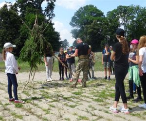 Dzieci znajdują się na świeżym powietrzu, uczą się jak prawidłowo zbudować trójnóg.