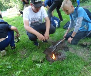 Dzieci znajdują się na polanie i kopią dołki, w których rozpalają ogień.