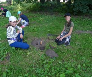 Dzieci znajdują się na polanie i kopią dołki, w których rozpalają ogień.