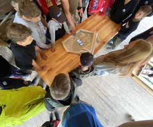 Dzieci stoją w kręgu i przyglądają się na leżącą na sole mapę.