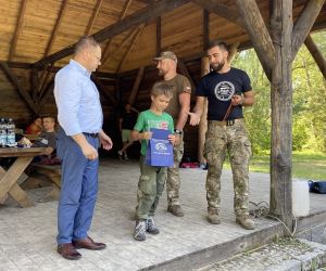Uczestnik spotkania odbiera nagrodę, która wręcza Sekretarz Gminy Hrubieszów, radny oraz prowadzący survival.