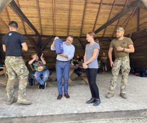 Uczestnik spotkania odbiera nagrodę, która wręcza Sekretarz Gminy Hrubieszów, radny oraz prowadzący survival.