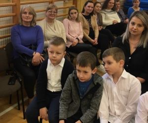 Uczniowie siedzą na ławkach obok nauczycieli