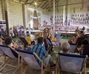 Zdjęcie przedstawia publiczność na koncercie, który odbywa się w stodole, a na środku panią, która gra na misach.