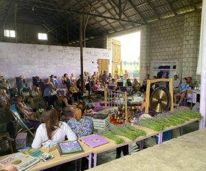 Zdjęcie przedstawia publiczność na koncercie, który odbywa się w stodole, a na środku panią, która gra na misach.