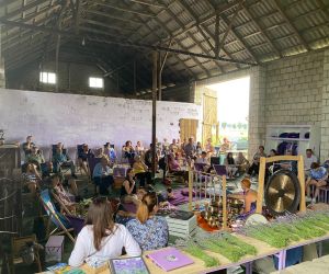 Zdjęcie przedstawia publiczność na koncercie, który odbywa się w stodole, a na środku panią, która gra na misach.