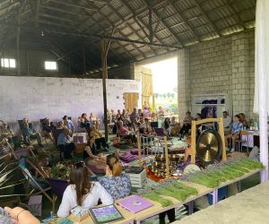 Zdjęcie przedstawia publiczność na koncercie, który odbywa się w stodole, a na środku panią, która gra na misach.