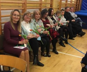 Panie nauczycielki siedzą w rzędzie, trzymając kwiaty w dłoniach
