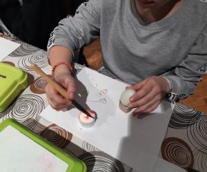 Uczennica ozdabia jajko woskiem pszczelim