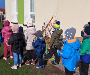 Dzieci idą w szeregu niosąc wiosenną gałąź.