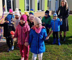 Dzieci idą w szeregu niosąc wiosenną gałąź.