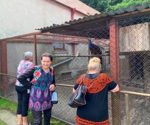 Zdjęcie przedstawia grupę ludzi na świeżym powietrzu  przed klatką z ptakami.