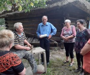 Zdjęcie przedstawia grupę osób na świeżym powietrzu zgromadzonych wokół mężczyzny, który lepi garnki.