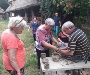 Zdjęcie przedstawia osobę znajdująca się na świeżym powietrzu, która lepi garnek z gliny.