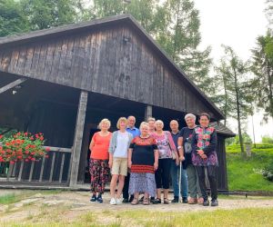 Zdjęcie przedstawia grupę ludzi na świeżym powietrzu na tle kapliczki na wodzie.